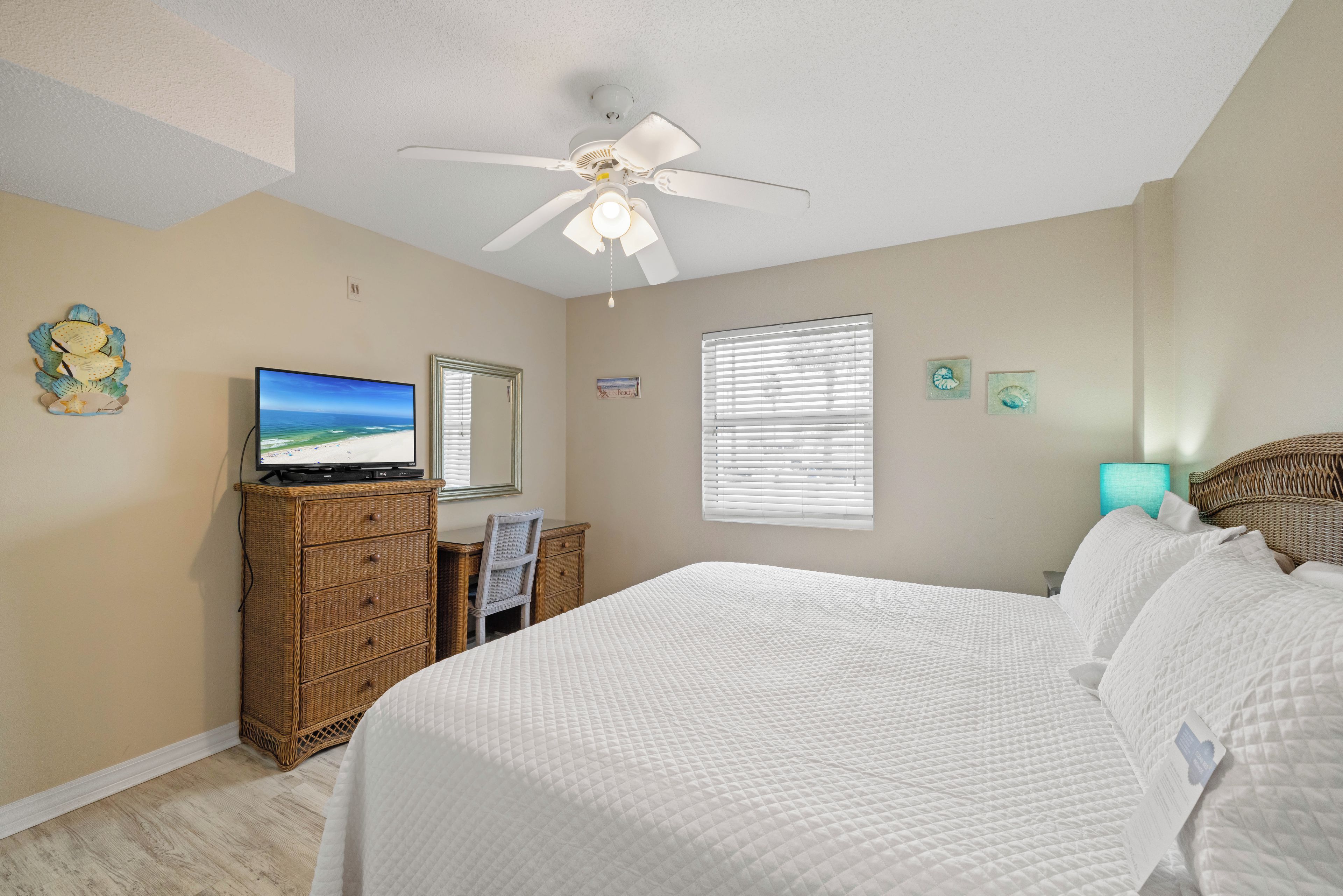 A bedroom with a bed, a television on a dresser, a ceiling fan, and a window with blinds.