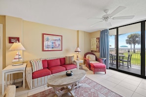A living room with a sofa, a coffee table, a chair, a lamp, and a ceiling fan. - Sunswept 108 by Liquid Life (Orange Beach)