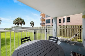 A patio with a table and chairs, a wooden fence, and a building with a balcony in the background. - Sunswept 108 by Liquid Life (Orange Beach)