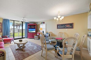 A spacious living room with a glass dining table, comfortable seating, a ceiling fan, and a view of the outdoors. - Sunswept 108 by Liquid Life (Orange Beach)