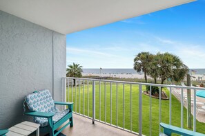 A balcony with a view of the beach, a grassy area, and a poolside area with chairs and umbrellas. - Sunswept 202 by Liquid Life (Orange Beach)