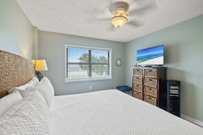 A bedroom with a bed, a television, a window with blinds, and a ceiling fan. - Sunswept 202 by Liquid Life (Orange Beach)