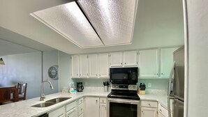 A modern kitchen with white cabinets, stainless steel appliances, and a light wood floor. - Sunswept 202 by Liquid Life (Orange Beach)