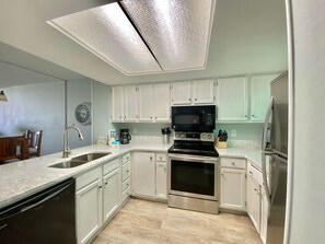 A modern kitchen with white cabinets, stainless steel appliances, and a light wood floor. - Sunswept 202 by Liquid Life (Orange Beach)