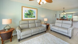 A living room with two sofas, a ceiling fan, a framed picture, and a kitchen in the background. - Sunswept 202 by Liquid Life (Orange Beach)