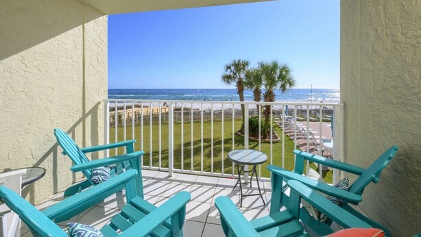 A balcony with turquoise chairs and a small table, overlooking a beach with palm trees and the ocean. - Sunswept 202 by Liquid Life (Orange Beach)