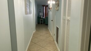A hallway with a tiled floor, a door with a vent, and a small table with a lamp. - Sunswept 204 by Liquid Life (Orange Beach)