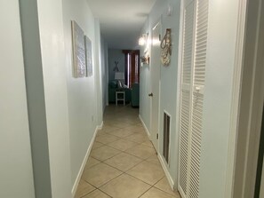 A hallway with a tiled floor, a door with a vent, and a small table with a lamp. - Sunswept 204 by Liquid Life (Orange Beach)