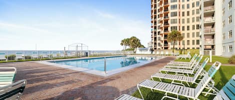 A swimming pool with lounge chairs and a high-rise building in the background.