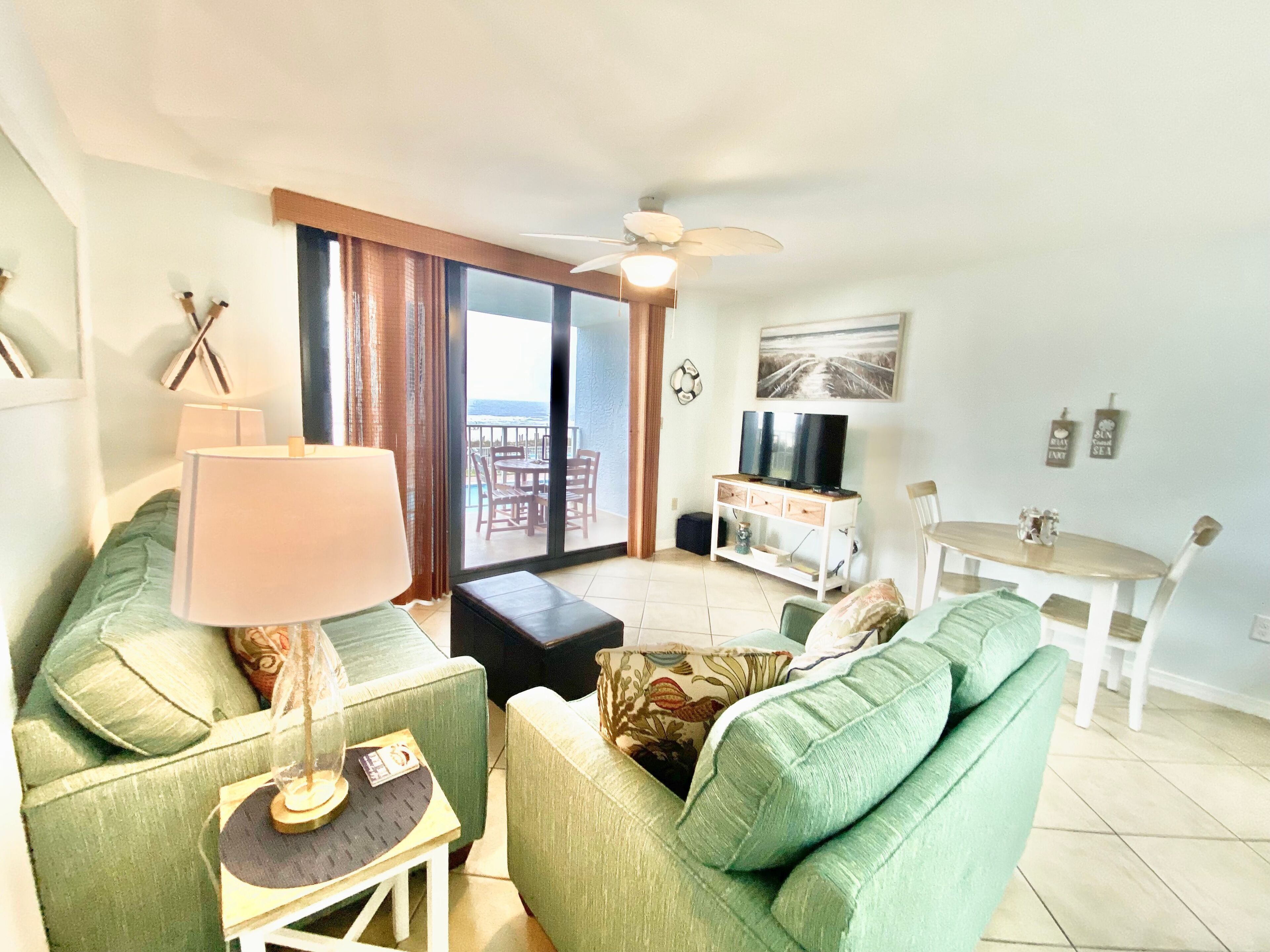 Ein Wohnzimmer mit einer Couch, einem Tisch, einer Lampe, einem Fernseher und einem Balkon mit Blick.