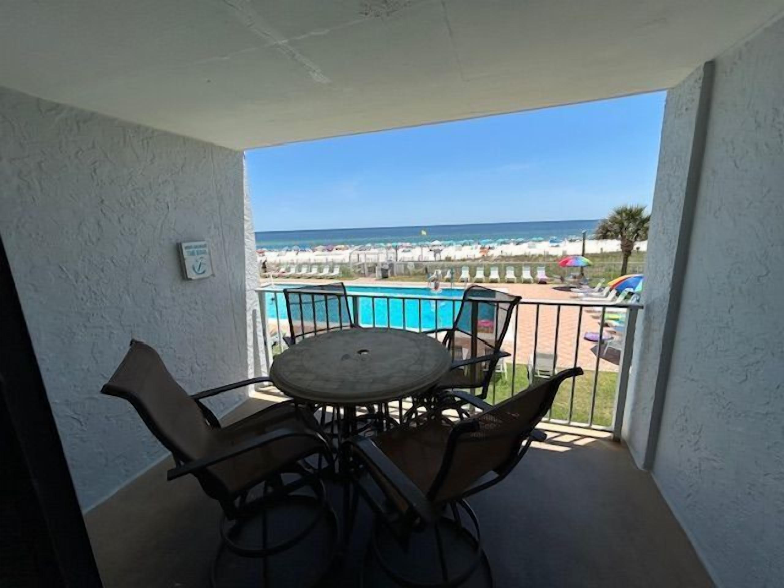 Ein Balkon mit Tisch und Stühlen, mit Blick auf Pool und Strand.