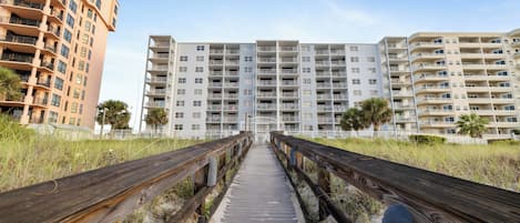 A wooden boardwalk leading to a beachfront residential area with multi-story buildings.