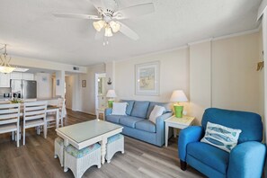 Ein Wohnzimmer mit einem blauen Sofa, einem weißen Couchtisch und einem Deckenventilator.