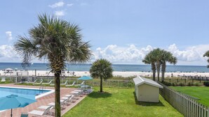 A pool area with lounge chairs and umbrellas, a small shed, and a view of the beach. - Sunswept 208 by Liquid Life (Orange Beach)