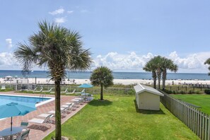 A pool area with lounge chairs and umbrellas, a small shed, and a view of the beach. - Sunswept 208 by Liquid Life (Orange Beach)
