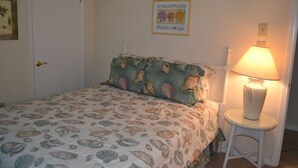 A bedroom with a bed covered in a seashell patterned bedspread, a bedside lamp, and a framed picture on the wall. - Sunswept 208 by Liquid Life (Orange Beach)