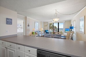 Eine moderne Küche mit eingebautem Geschirrspüler, ein Essbereich mit Blick auf den Strand und ein Wohnzimmer mit Deckenventilator und großem Fenster.