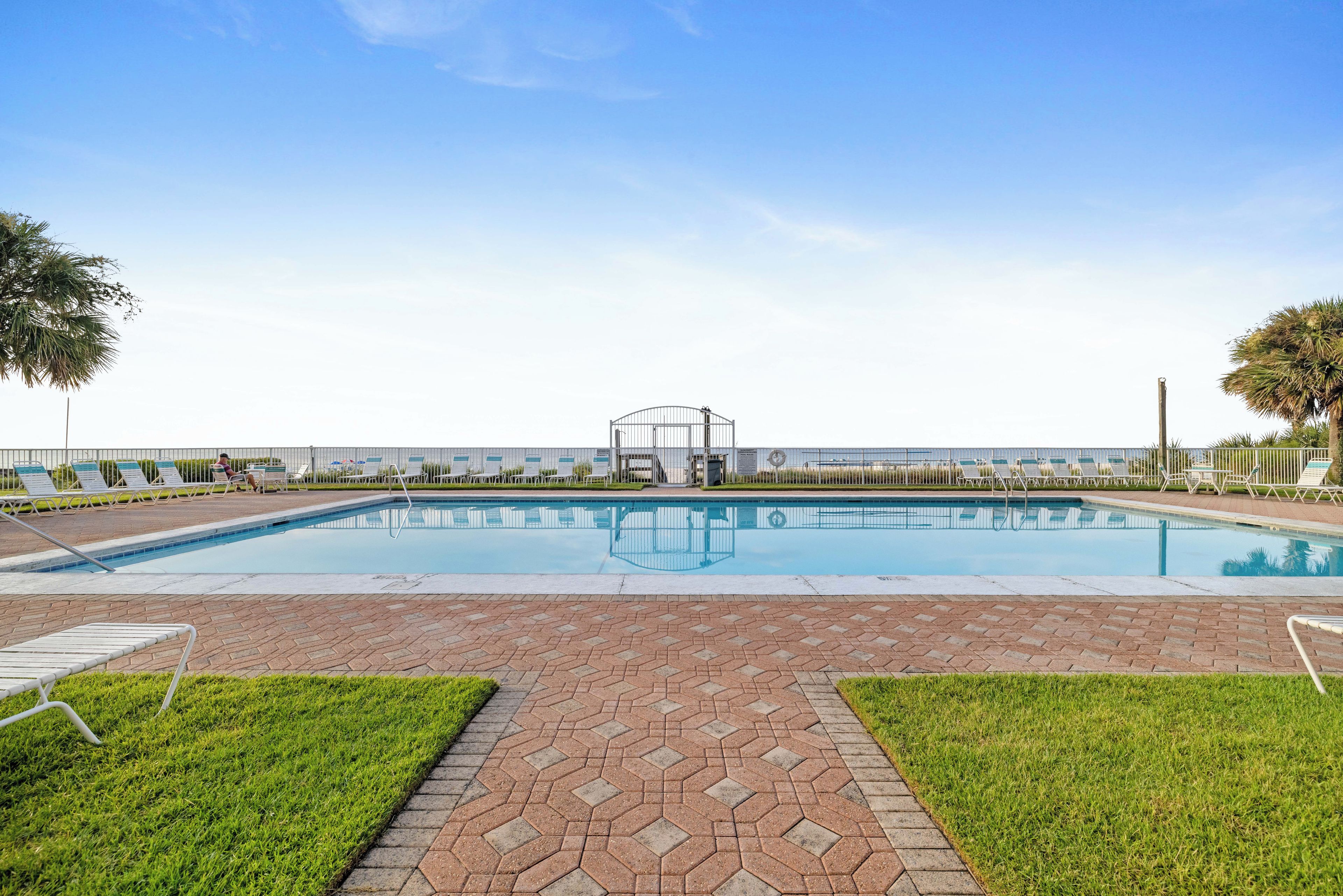 A rectangular swimming pool with a clear blue water surface, surrounded by a paved walkway with a herringbone pattern.