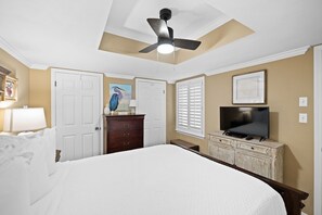 A bedroom with a bed, dresser, television, ceiling fan, and artwork on the walls. - Sunswept 304 by Liquid Life (Orange Beach)