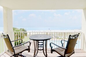 A balcony with a table and two chairs, overlooking a beach and a pool. - Sunswept 304 by Liquid Life (Orange Beach)