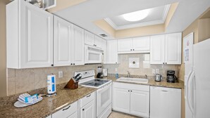A modern kitchen with white cabinetry, a granite countertop, and a skylight. - Sunswept 304 by Liquid Life (Orange Beach)