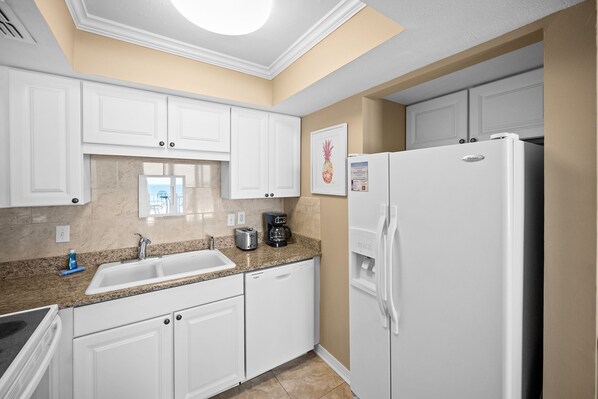 Una cocina con armarios blancos, un refrigerador blanco, una cafetera y un tostador.