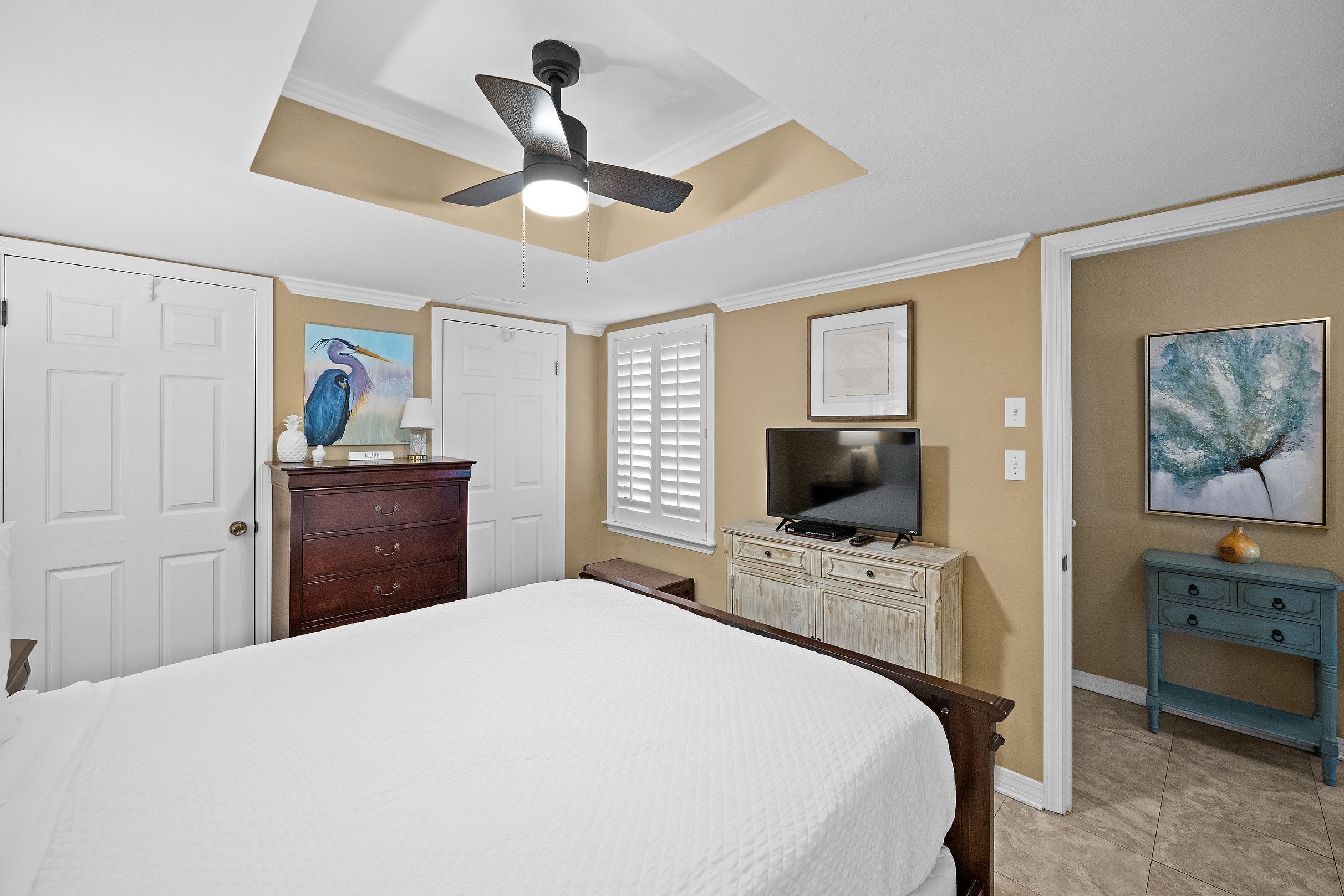 A bedroom with a bed, a ceiling fan, a dresser, a television, and artwork on the walls.