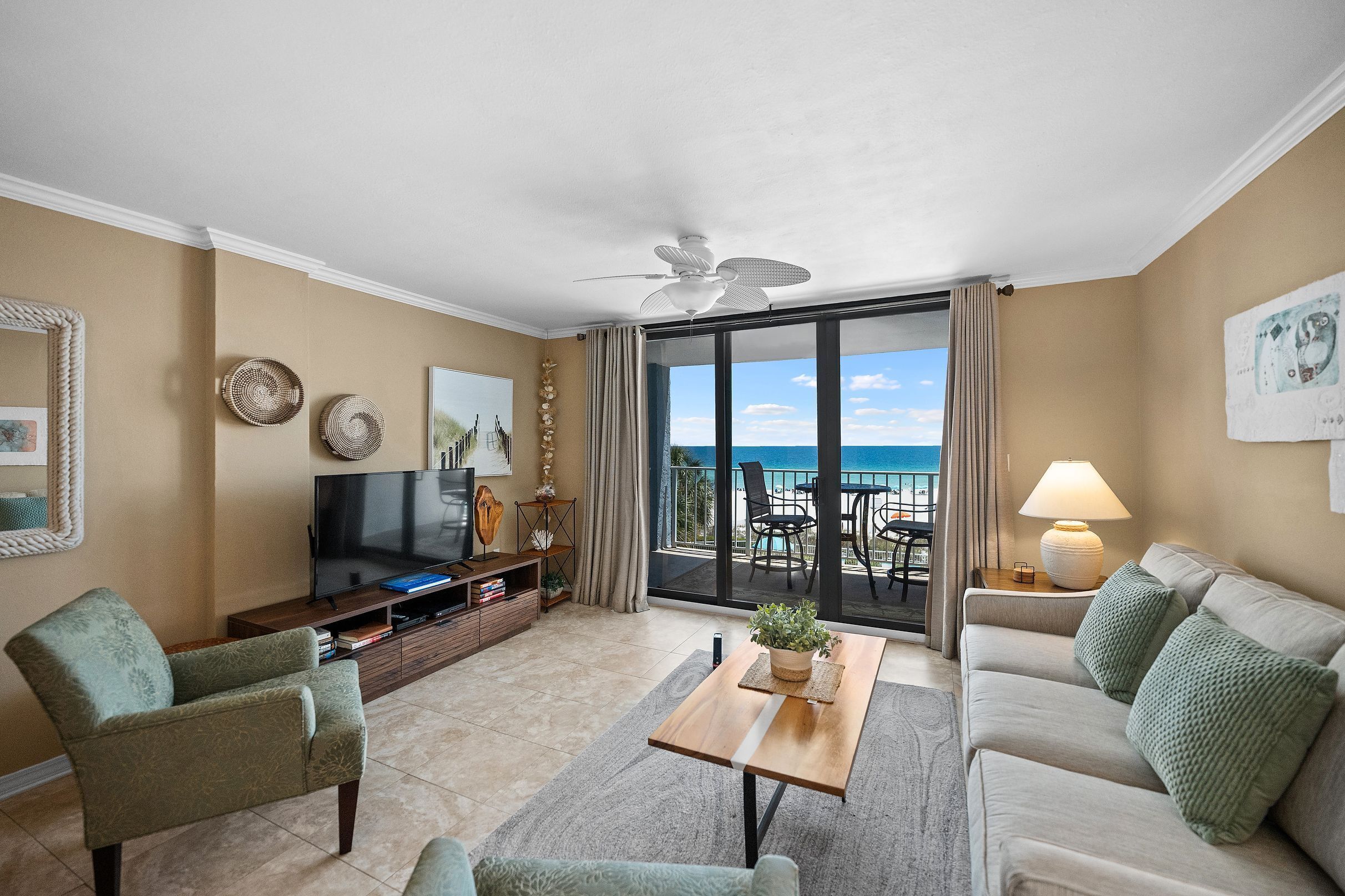 A living room with a television, seating, a coffee table, and a view of the ocean.