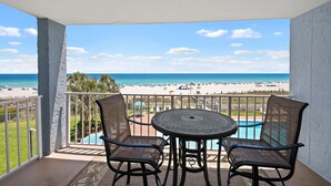 A balcony with two chairs and a table, overlooking a beach and a pool. - Sunswept 304 by Liquid Life (Orange Beach)
