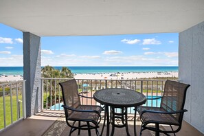 A balcony with two chairs and a table, overlooking a beach and a pool. - Sunswept 304 by Liquid Life (Orange Beach)