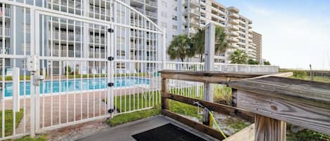 Un edificio moderno de varios pisos con una zona de piscina, que incluye una terraza de madera y una cerca metálica.