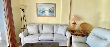 A living room with a sofa, a chair, a lamp, and a painting on the wall.