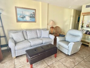 A living room with a sofa, a chair, an ottoman, a painting, a lamp, and a bookshelf. - Sunswept 305 by Liquid Life (Orange Beach)