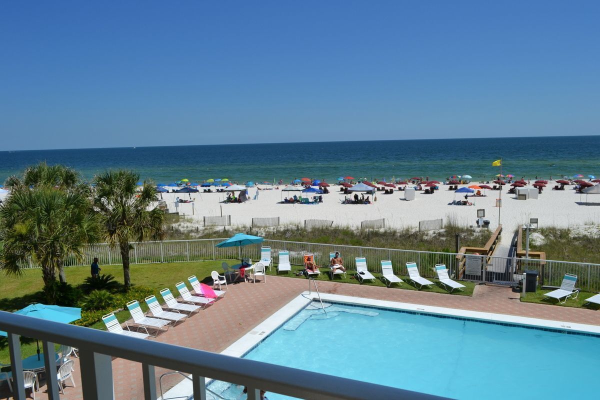 A poolside area with lounge chairs and umbrellas, a clear view of the beach, and a flag.