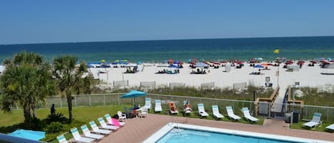 A poolside area with lounge chairs and umbrellas, a clear view of the beach, and a flag.