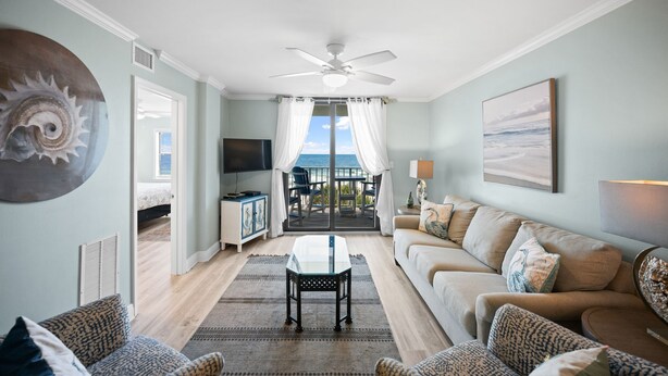 A living room with a view of the ocean, a ceiling fan, a TV, and a sofa. - Sunswept 402 by Liquid Life (Orange Beach)
