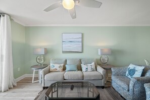 A living room with a ceiling fan, two lamps, a sofa set, a coffee table, and a patterned rug. - Sunswept 402 by Liquid Life (Orange Beach)