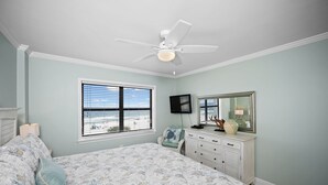 A bedroom with a bed, a dresser, a ceiling fan, a window with a beach view, and a television. - Sunswept 402 by Liquid Life (Orange Beach)