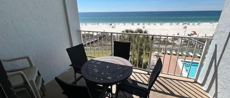 Een balkon met een tafel en stoelen, met uitzicht op een strand en een zwembad.