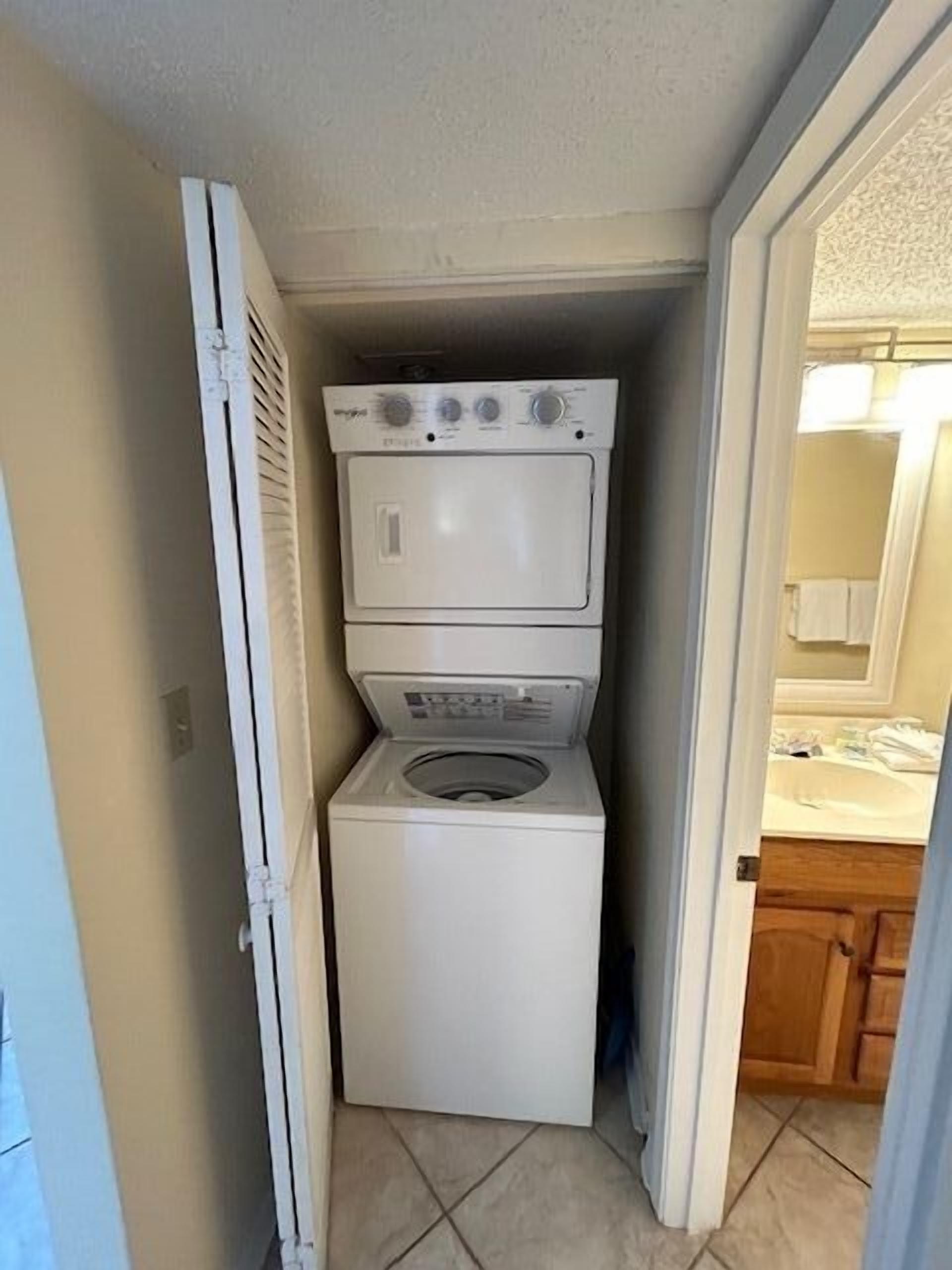 A laundry room with stacked appliances, a door leading to a bathroom, and a tiled floor.