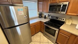A kitchen with stainless steel appliances, wooden cabinets, and a tiled floor. - Sunswept 403 by Liquid Life (Orange Beach)