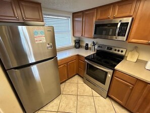 A kitchen with stainless steel appliances, wooden cabinets, and a tiled floor. - Sunswept 403 by Liquid Life (Orange Beach)