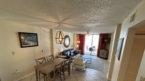 A dining area with a table and chairs, a sofa, and a television in the background. - Sunswept 403 by Liquid Life (Orange Beach)
