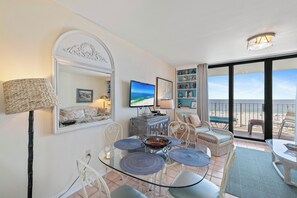 A room with a glass table, wicker chairs, a television, and a view of the beach. - Sunswept 405 by Liquid Life (Orange Beach)