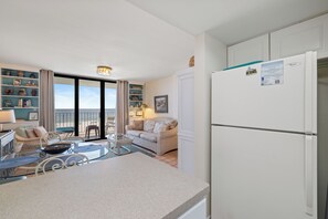 A modern kitchen with a built-in refrigerator, a dining area with a glass table, and a balcony with a view of the beach. - Sunswept 405 by Liquid Life (Orange Beach)