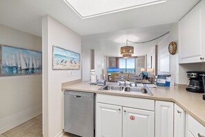 A modern kitchen with a dishwasher, a coffee maker, and a view of the living area. - Sunswept 406 by Liquid Life (Orange Beach)