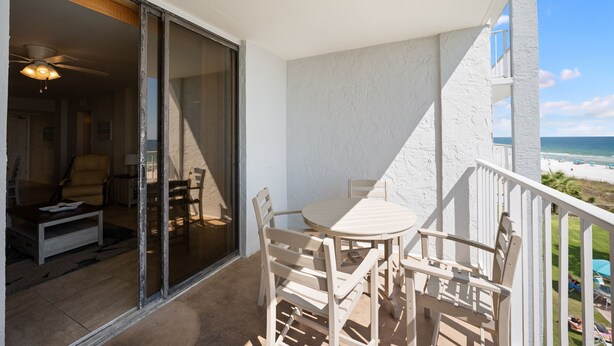 A balcony with a table and chairs, a sliding glass door leading to an interior room, and a view of the beach. - Sunswept 406 by Liquid Life (Orange Beach)