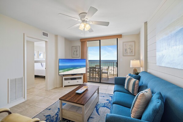 Une chambre d’hôtel avec un balcon, une télévision, un canapé bleu et un ventilateur de plafond.