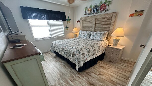 Une chambre à coucher comprenant un lit, des tables de chevet, un bureau et une fenêtre avec des stores.