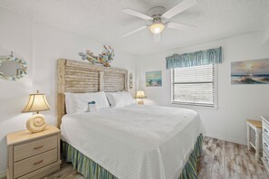 A bedroom with a bed, nightstands, a ceiling fan, a window with blinds, and wall art. - Sunswept 407 by Liquid Life (Orange Beach)